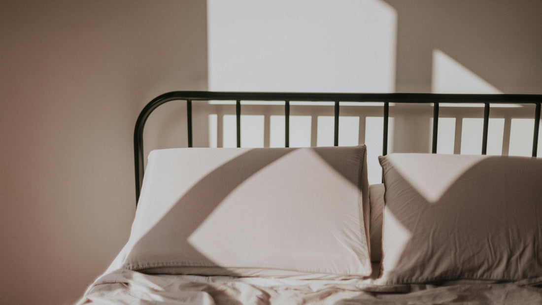 Soft morning sunlight casting geometric shadows across the pillows and sheets of an iron-frame bed.